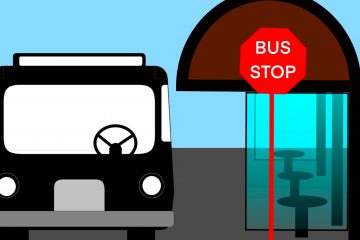 Looking at the front of a city bus stopped at a glass-enclosed bus stop with a red sign with white text spelling “Bus Stop.”