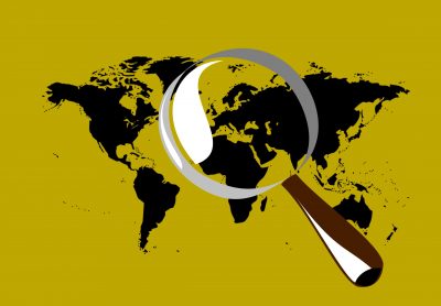 An image of the world map on a yellow background and with a giant magnifying glass over the middle of the map.