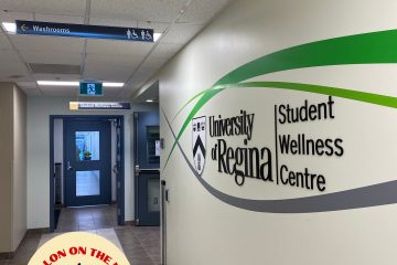 A photo of a wall with the words “University of Regina Student Wellness Centre” on it. 