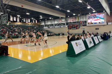 A photo of the University of Regina and Fraser Valley’s women’s basketball teams playing a match. The players are focused on the basketball in the air. The score is 33:25 in Fraser Valley’s favour.